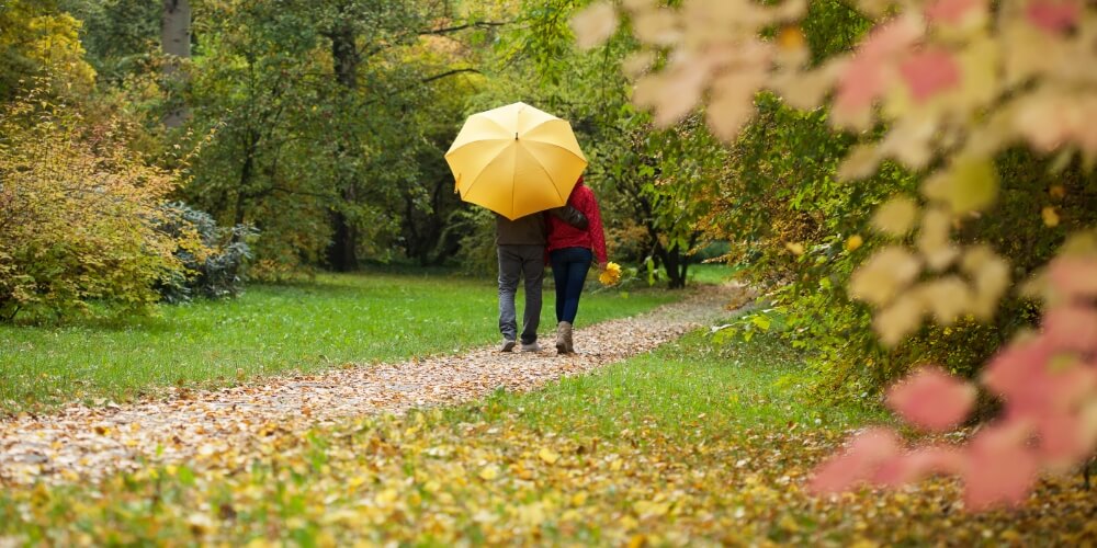 A couple walking with a yellow umbrella.